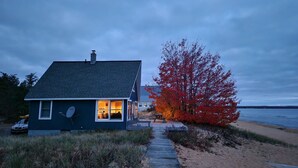 Una casa con antena parabólica, una terraza de madera y una playa al fondo.