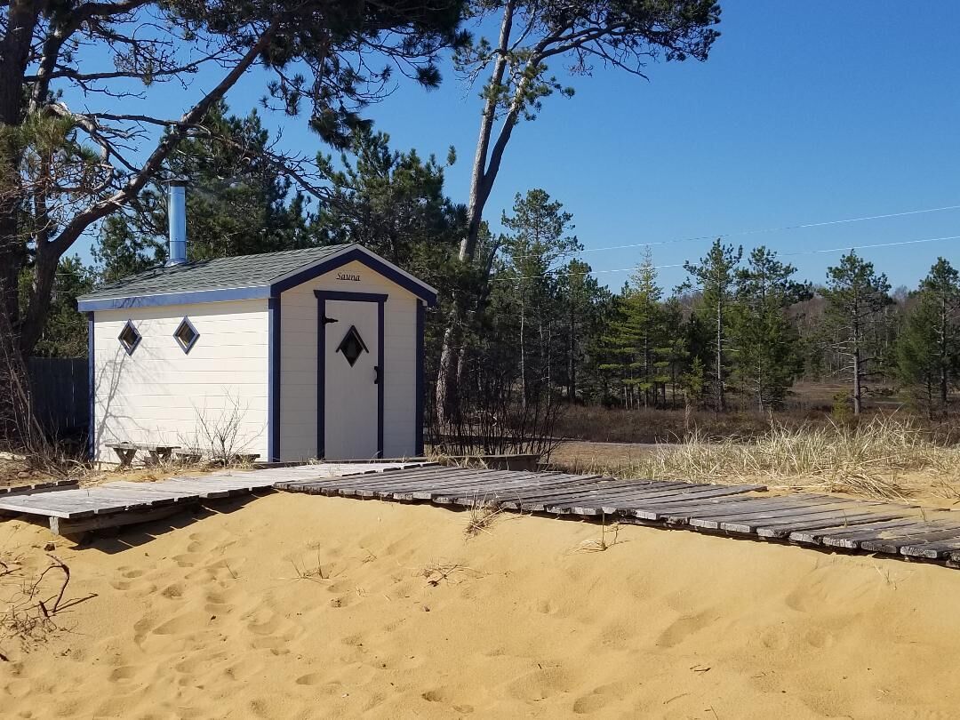 Eine kleine Holzhütte mit Tür und Fenstern, umgeben von Sand und Bäumen.