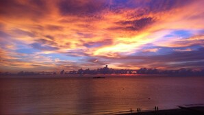Solnedgang over et roligt hav med en fjerntliggende kystlinje og et par personer på stranden.