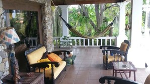 Un patio cubierto con paredes de piedra, una hamaca, mobiliario de mimbre y suelo de baldosas.