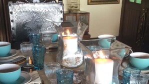 Una mesa de comedor dispuesta con cristalería y platos azules, un candelabro y una jaula de pájaros sobre un mantel decorado.