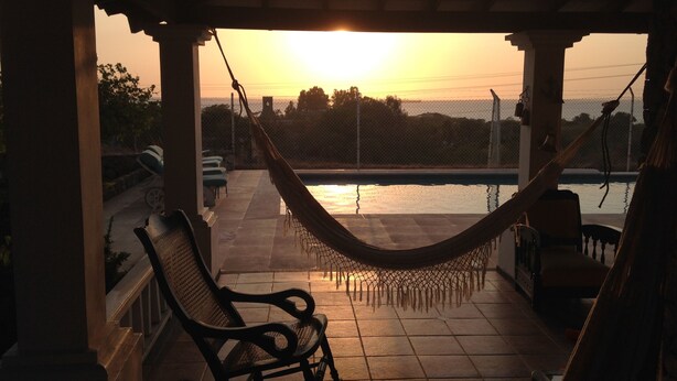 Una hamaca en un porche techado con vista a una piscina.