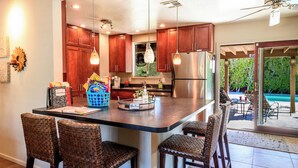 A kitchen with wooden cabinets, a stainless steel refrigerator, and a bar area with wicker chairs. - Charming Family Friendly Home with Heated Pool.   (Palm Springs)