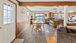 Una cocina amplia con gabinetes de madera, un comedor con una mesa grande y sillas, y vistas a un lago a través de las ventanas.