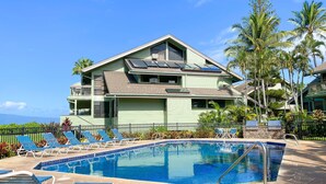 Ein Poolbereich mit Liegestühlen und einem Gebäude mit geneigtem Dach und Solaranlagen.
