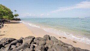 Ein Strand mit felsigem Vordergrund, klarem Wasser und weiter Aussicht auf den Ozean.