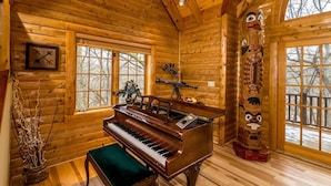 A wooden cabin interior with a grand piano, large windows, and a decorative totem. - Wildlife Surrounds! Enjoy Fireplace, Pool Table, Fire Pit, Piano. Near Marina! (Galena)