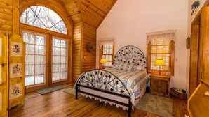 A log cabin bedroom with a large bed, wooden floors, and a window with a view of trees. - Wildlife Surrounds! Enjoy Fireplace, Pool Table, Fire Pit, Piano. Near Marina! (Galena)