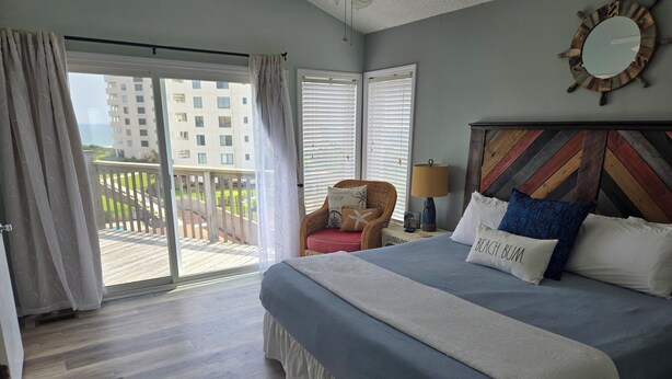 Ein Schlafzimmer mit einem großen Bett, einem Sessel, einer Lampe und Blick auf einen Balkon.