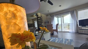 Ein modernes Wohnzimmer mit einem großen Fenster, einem Deckenventilator und einem Fernseher.