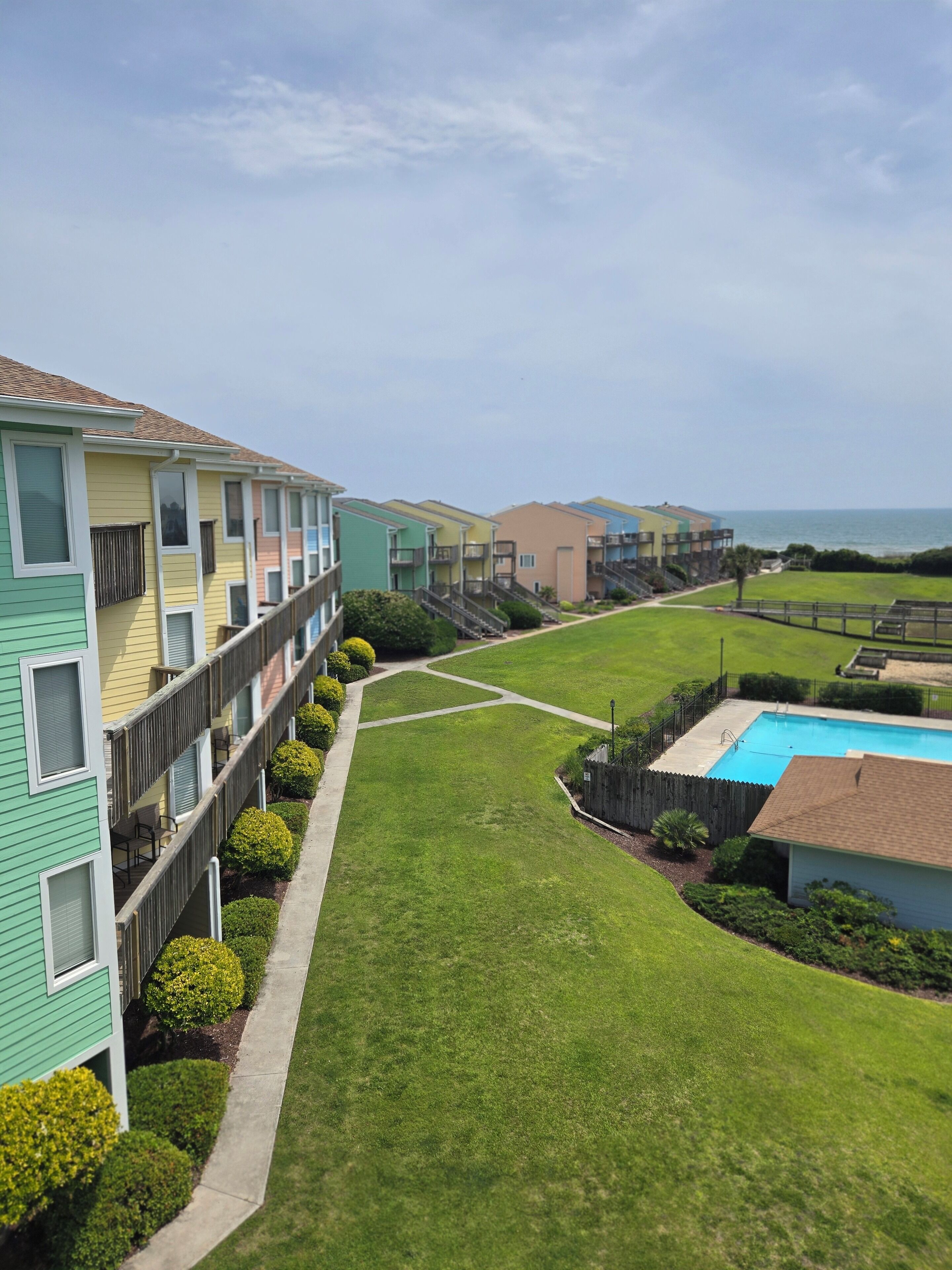A row of colorful apartment buildings with a swimming pool and a well-maintained lawn.