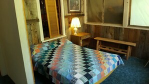 Une petite pièce rustique avec un lit en bois, une table de chevet avec une lampe et un banc.
