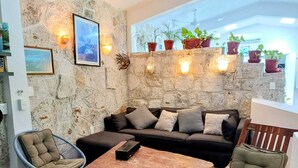 A cozy outdoor seating area with a stone wall, a sofa, two chairs, a table, and potted plants.