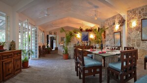 A spacious dining area with a high ceiling, stone walls, and multiple potted plants.