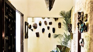 A hallway with a stone floor, a wooden door, and a wall decorated with various artifacts and a potted plant.