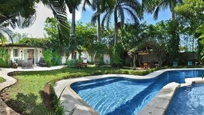 A swimming pool surrounded by lush greenery and a small patio area with outdoor furniture.