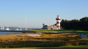 En golfbana vid kusten med en fyr, en småbåtshamn och ett klubbhus.