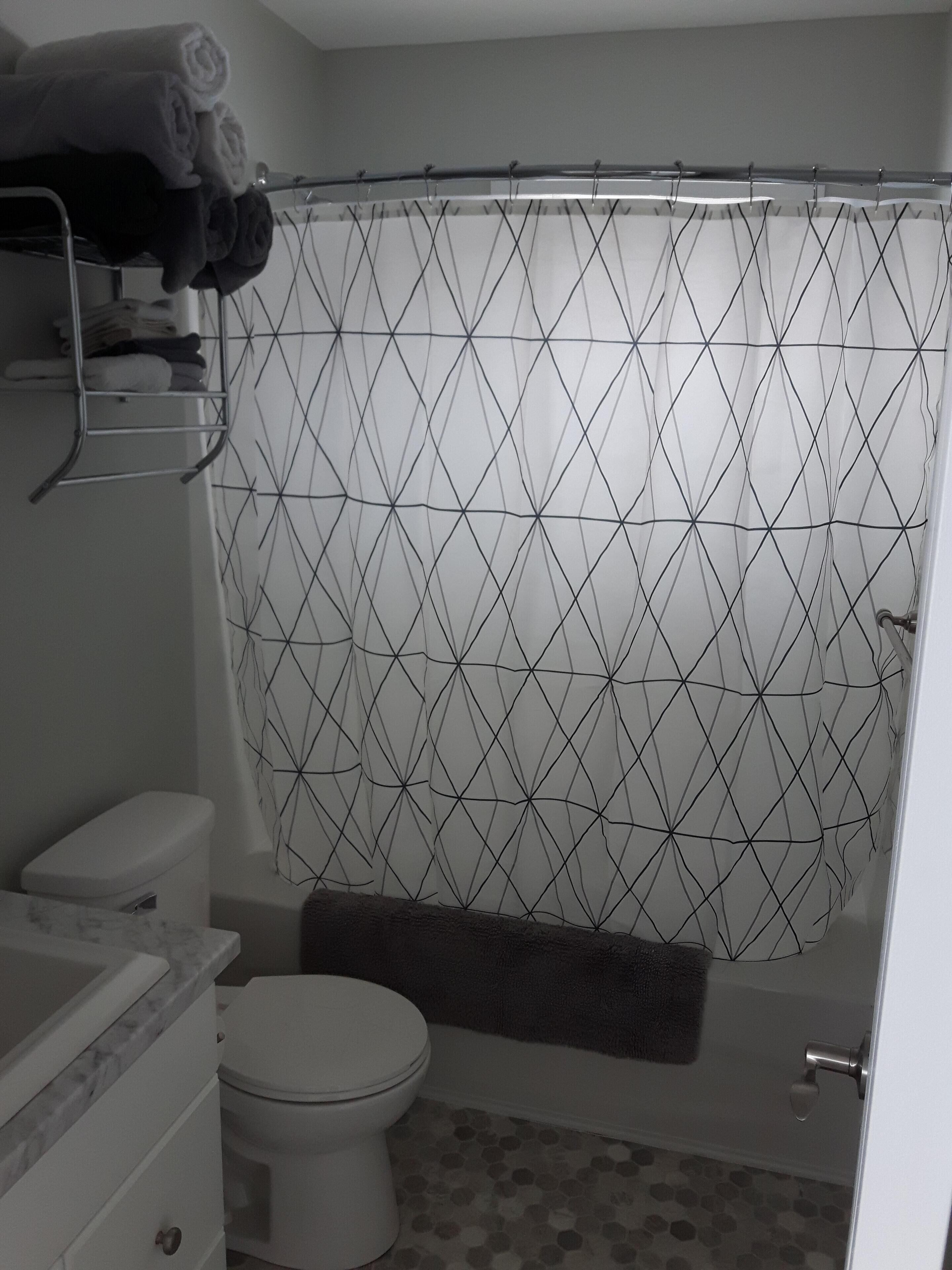 Ein Badezimmer mit Duschvorhang mit geometrischem Muster, Toilette und Marmorwaschbecken.