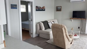 A modern living room with a sofa, a recliner, a TV on a stand, and a wall-mounted air conditioner. - 2 bedroom, A/C, Sleeps 6 (New London)
