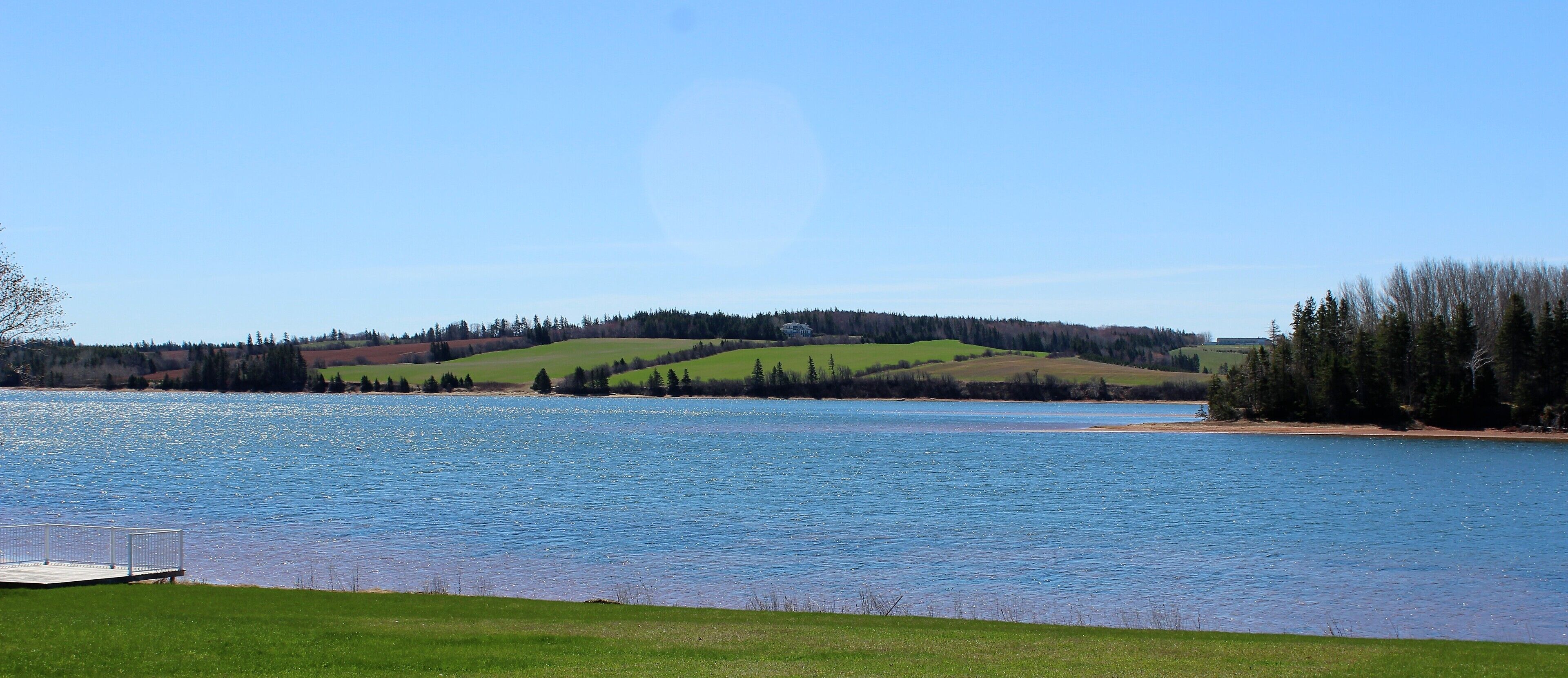 A lake with a dock, surrounded by green hills and trees.