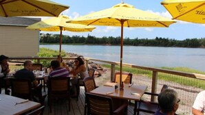 An outdoor dining area with yellow umbrellas, wooden tables, and chairs, overlooking a body of water. - 2 bedroom, A/C, Sleeps 6 (New London)