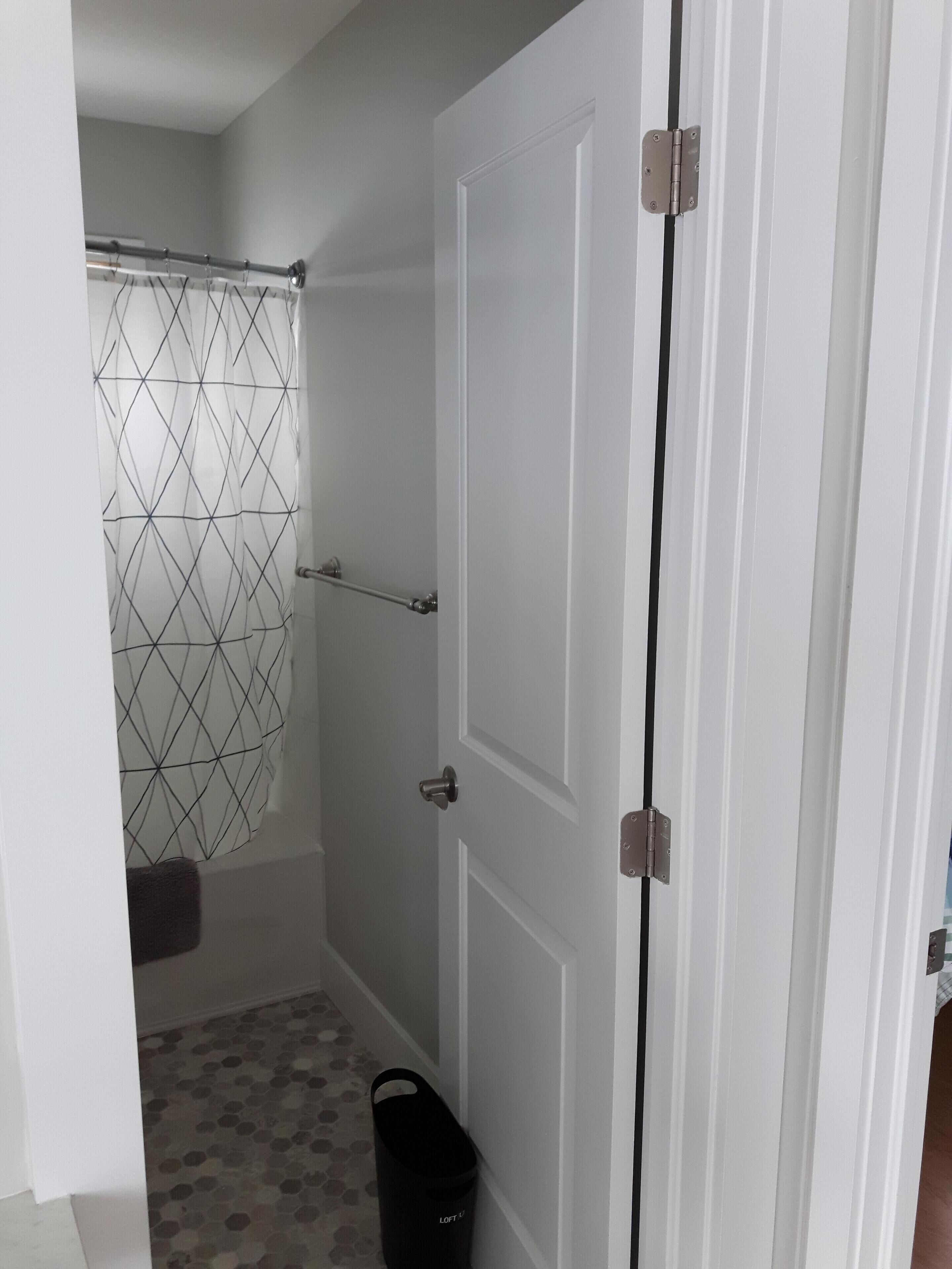 A bathroom with a shower curtain, a towel rack, and a trash bin.