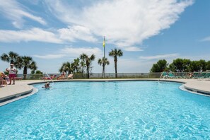 A swimming pool with clear blue water, surrounded by palm trees and lounge chairs.