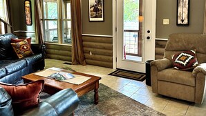 Un accogliente soggiorno con un divano in pelle, un tavolino in legno e una poltrona beige. Una porta con pannello in vetro dà accesso a una zona esterna.