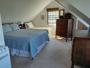 A bedroom with a large bed, a smaller bed, a dresser, and a window with blinds.