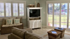 Sala de estar con un mueble de entretenimiento blanco, muebles de mimbre y vistas a través de grandes puertas correderas de vidrio.