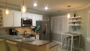Una cocina moderna con armarios blancos, una isla central con taburetes, un refrigerador y un microondas.