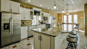 Una cocina moderna con una isla grande, electrodomésticos de acero inoxidable y un área de comedor con taburetes de bar.