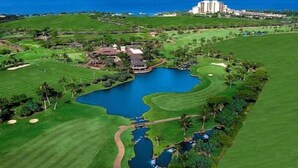 Un campo da golf con un grande stagno, un club house e un albergo sullo sfondo.