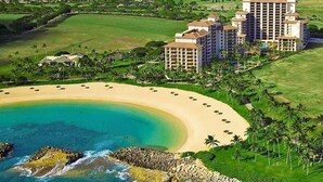 Vista aerea di un resort con spiaggia, diversi edifici a più piani e un'area verde curata.