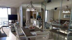 A dining area with a wooden table, white chairs, and a glass partition. - Upgraded and Renovated! Beach Chairs Included! Book Spring Break - Great Rates! (Panama City Beach)