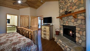 A bedroom with a bed, a stone fireplace, a television, and wooden doors. - Buss Stop (Wawona)