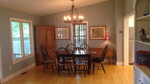 A dining room with a wooden table and chairs, a chandelier, and a window with blinds. - Carpenter St. Cottage In the Heart of St Michaels Village - Large Screened Porch (Saint Michaels)