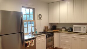 A kitchen with white cabinets, stainless steel appliances, a window, and a wooden floor. - Carpenter St. Cottage In the Heart of St Michaels Village - Large Screened Porch (Saint Michaels)
