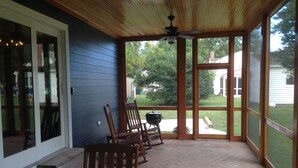 A covered porch with wooden chairs, a grill, and a view of a backyard. - Carpenter St. Cottage In the Heart of St Michaels Village - Large Screened Porch (Saint Michaels)
