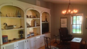 A room with a wooden cabinet, a television, a chair, and a chandelier. - Carpenter St. Cottage In the Heart of St Michaels Village - Large Screened Porch (Saint Michaels)