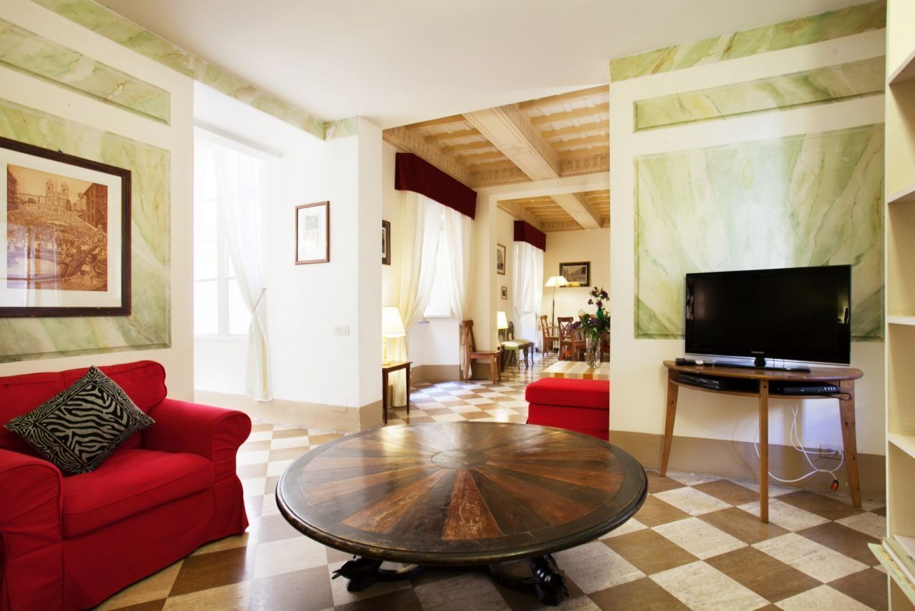 Ein geräumiges Wohnzimmer mit einem roten Sofa, einem runden Couchtisch und einem Fernseher auf einem Holzboden.