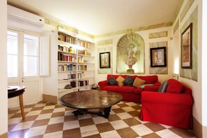 A living room with a checkered floor, a red sofa, a round coffee table, and a bookshelf filled with books.