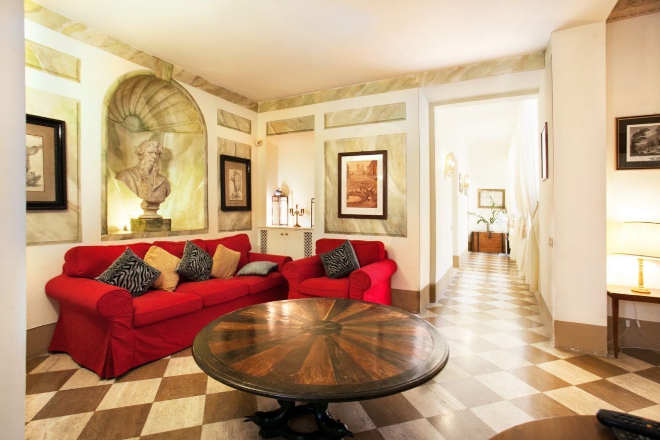 A spacious living area with a checkered floor, red sofas, and a central round table.