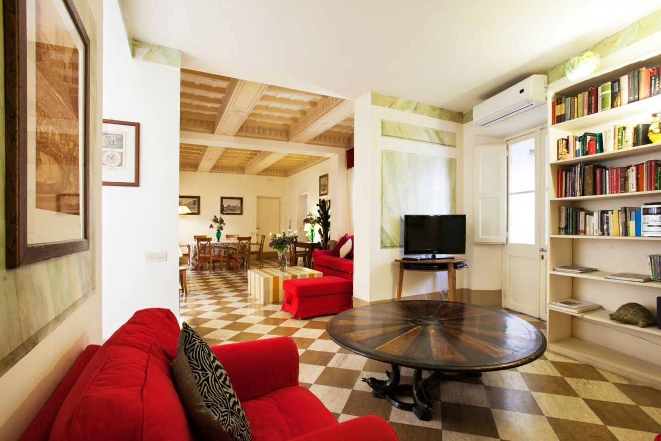 A living room with a checkered floor, a red sofa, a round coffee table, a television, and a bookshelf filled with books.