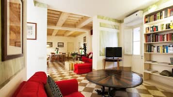A living room with a checkered floor, a red sofa, a round coffee table, a television, and a bookshelf filled with books.