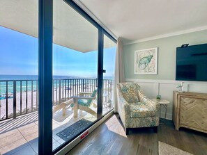 A room with a view of the beach, a chair, a small table, and a cabinet.