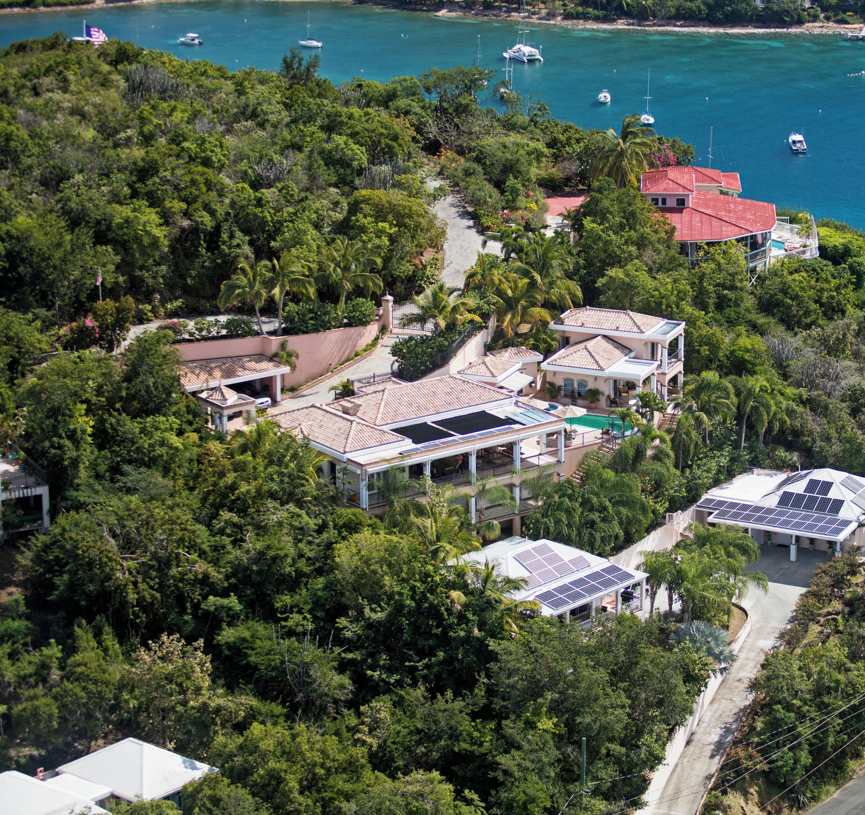 An aerial view of a coastal property with multiple buildings, a road, and a marina with boats.