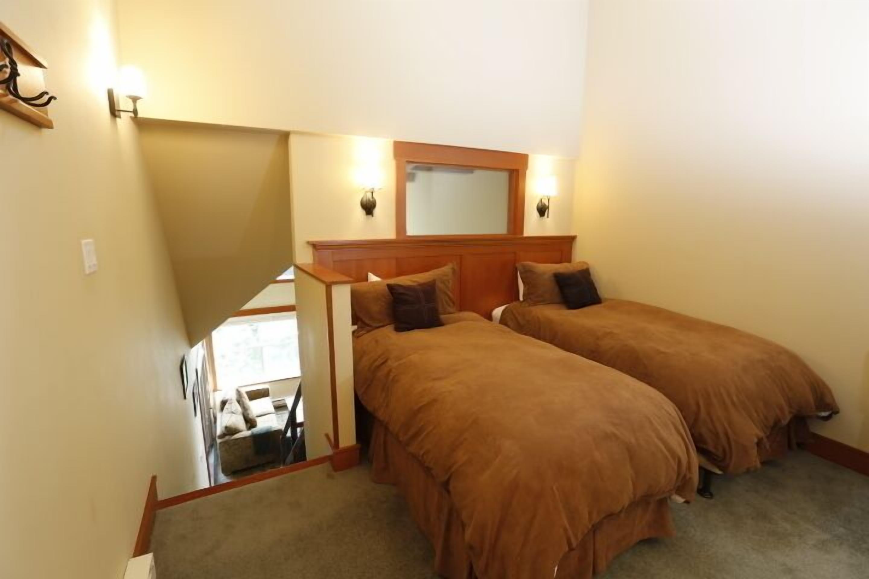 A bedroom with two single beds, a wooden headboard, a mirror above the beds, and a staircase leading to another room.