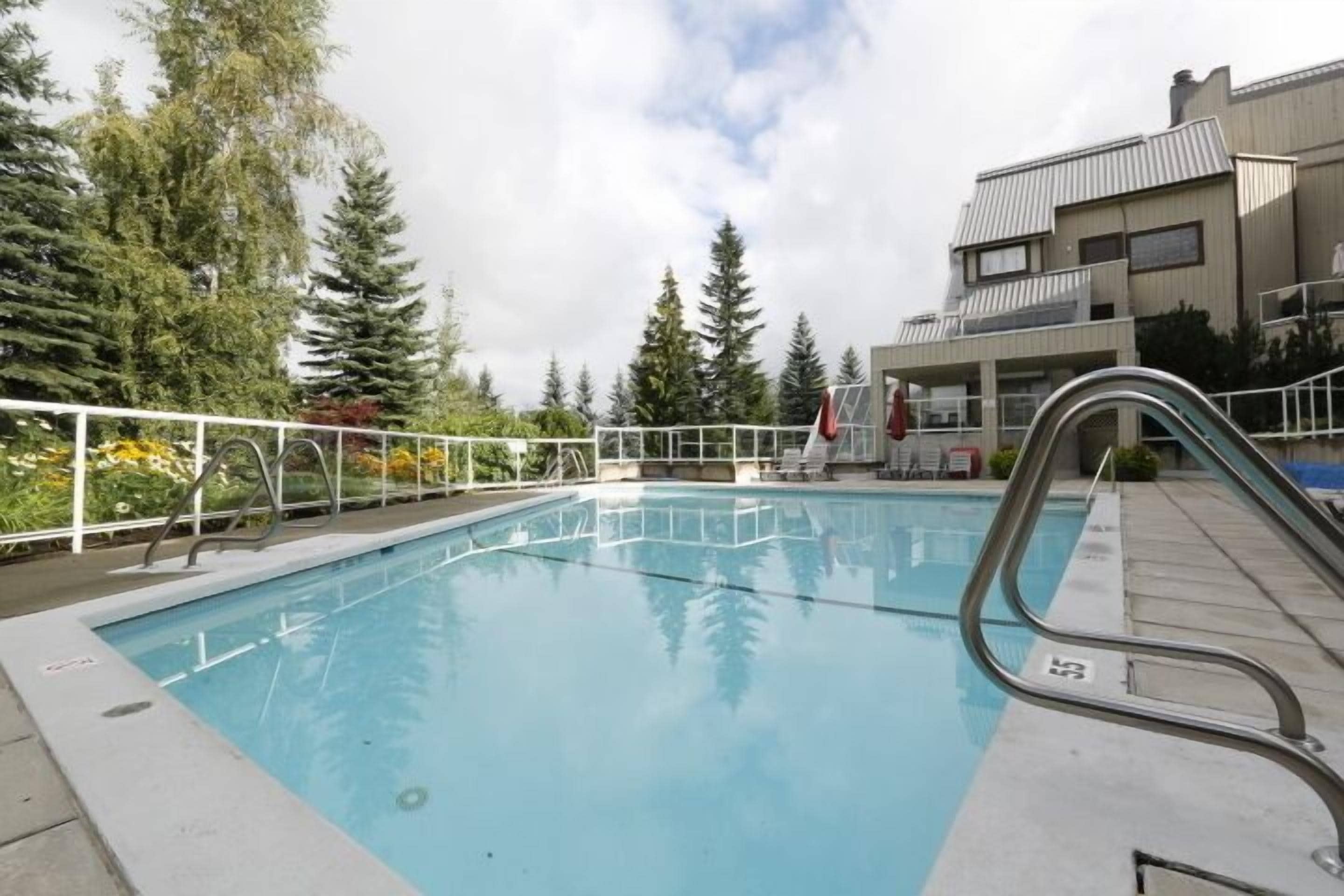 Piscina amb escala metàl·lica, envoltada per una tanca blanca i arbres.