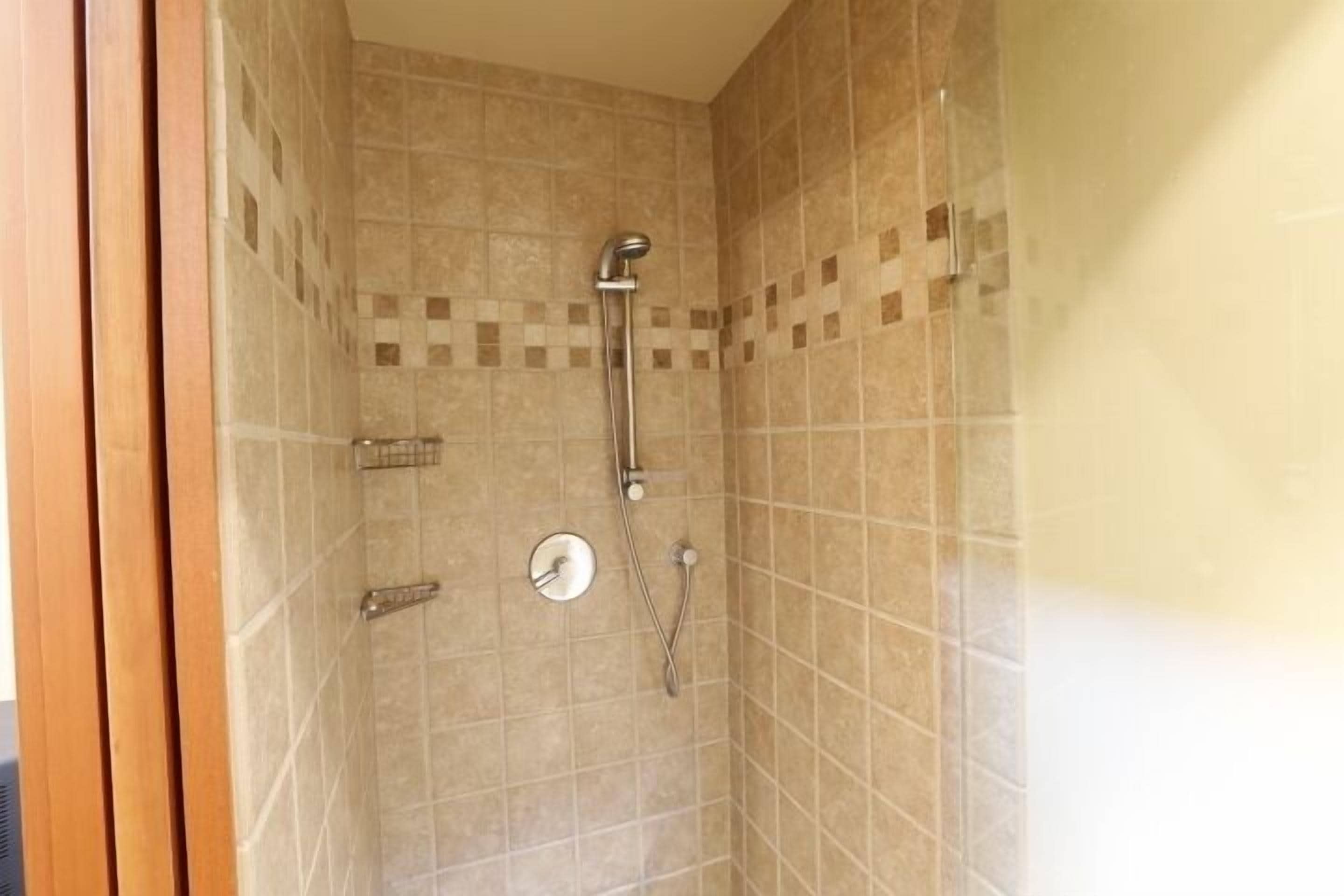 Pequeño espacio de ducha cerrado, con paredes de azulejos y ducha.